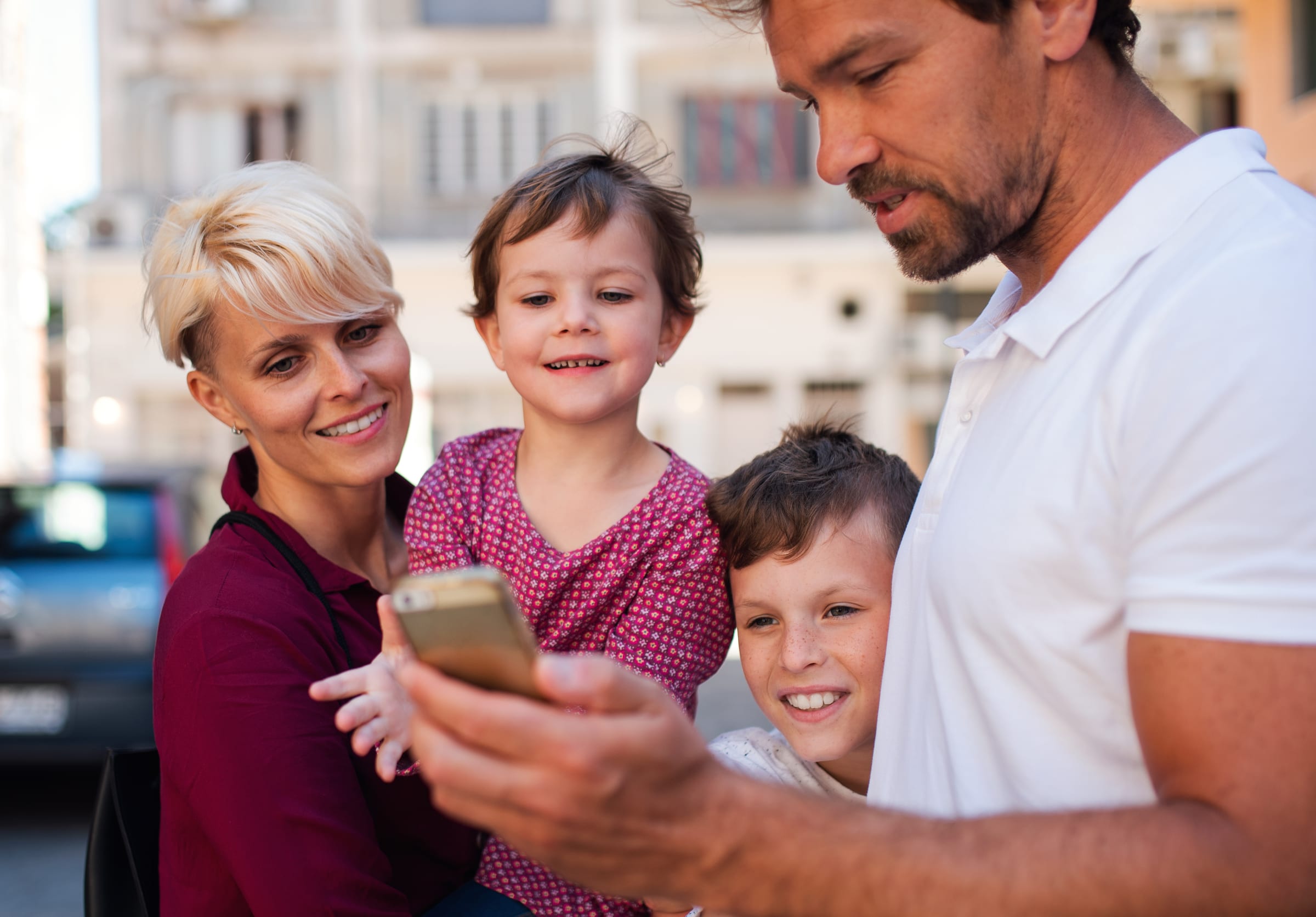 Deux parents et leurs deux enfants sourient en regardant ensemble un téléphone intelligent en ville.