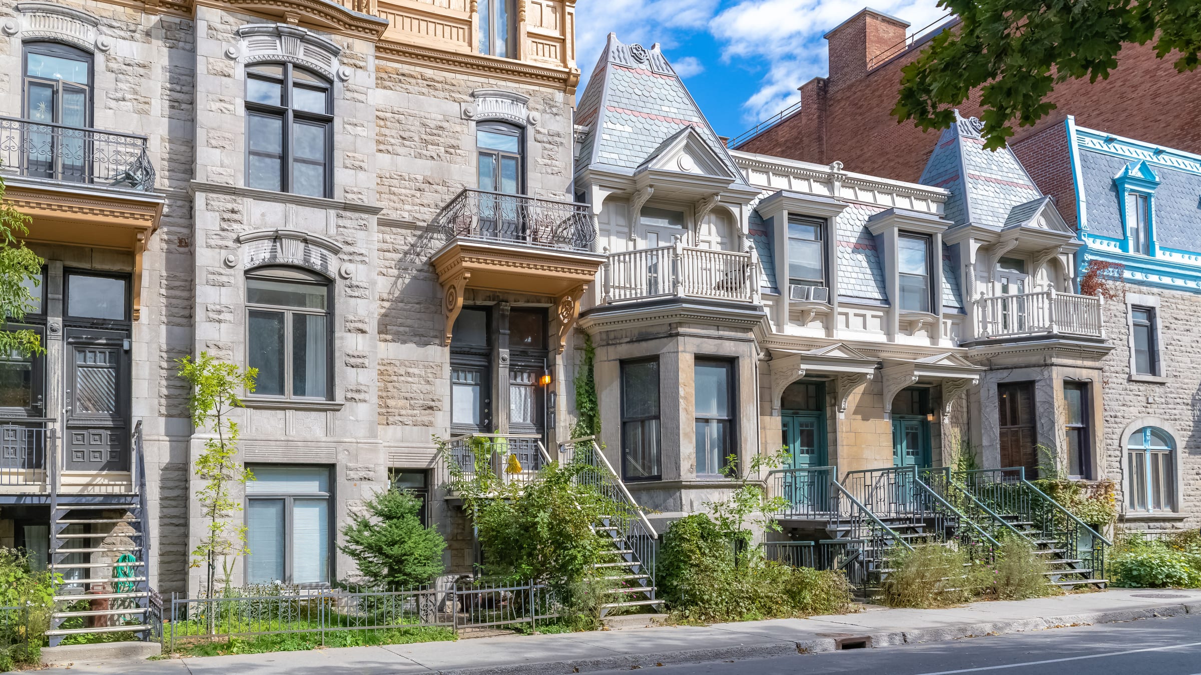 Des maisons victoriennes de Montréal bordent la rue, avec leurs balcons, escaliers extérieurs et jardins.